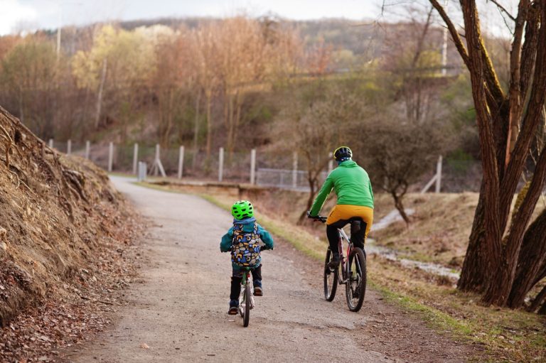Pappa och son i cykelhjälmar cyklar på en grusväg en tidig vårdag